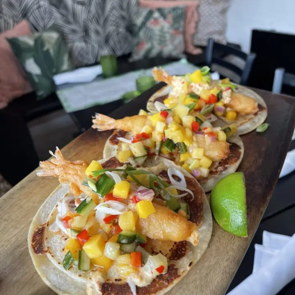 Three Salted. On The Harbor shrimp tacos with mango salsa and lime on a wooden board.