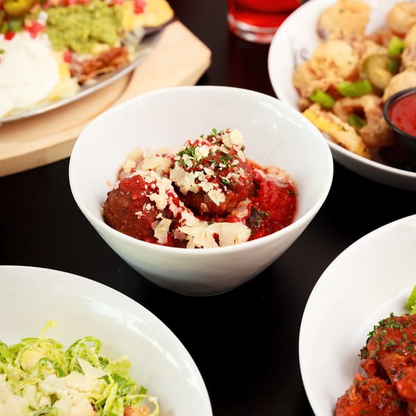A white bowl of meatballs with red sauce and parmesan cheese, surrounded by other dishes.