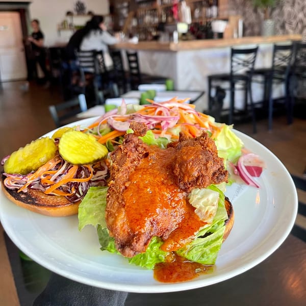 A fried chicken sandwich with pickles and slaw, served with a side salad at Salted. On The Harbor.